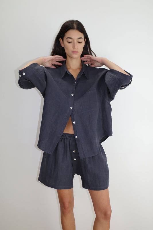 female model wears the 03 set by Deiji Studios in ink
features an oversized box fit linen shirt with wide arms and a front pocket designed to sit mid rise, the loose fitting boxer style shorts have a faux button down fly and an elastic waist for extra comfort
made from 100% GOTS certified organic, OEKO-TEX 100 certified and EU certified stone washed french linen