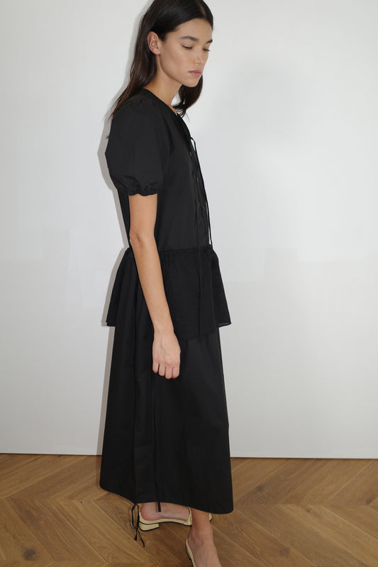female model wears the draw hem dress by Deiji Studios in black
elevated everyday dress in mid length features a flattering v neckline with tie, button front detail with a drop waist, and soft elastic blouson sleeve
made from 100% organic cotton poplin