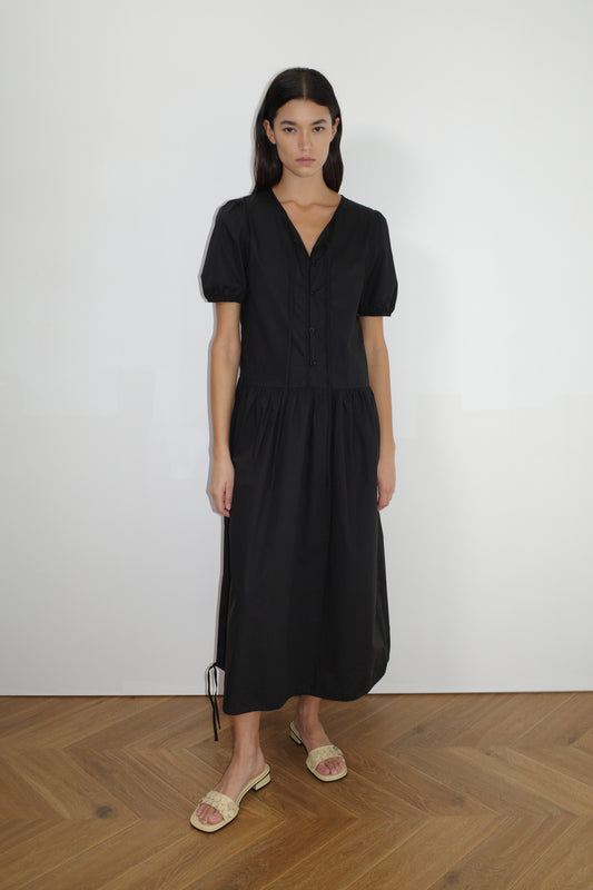 female model wears the draw hem dress by Deiji Studios in black
elevated everyday dress in mid length features a flattering v neckline with tie, button front detail with a drop waist, and soft elastic blouson sleeve
made from 100% organic cotton poplin