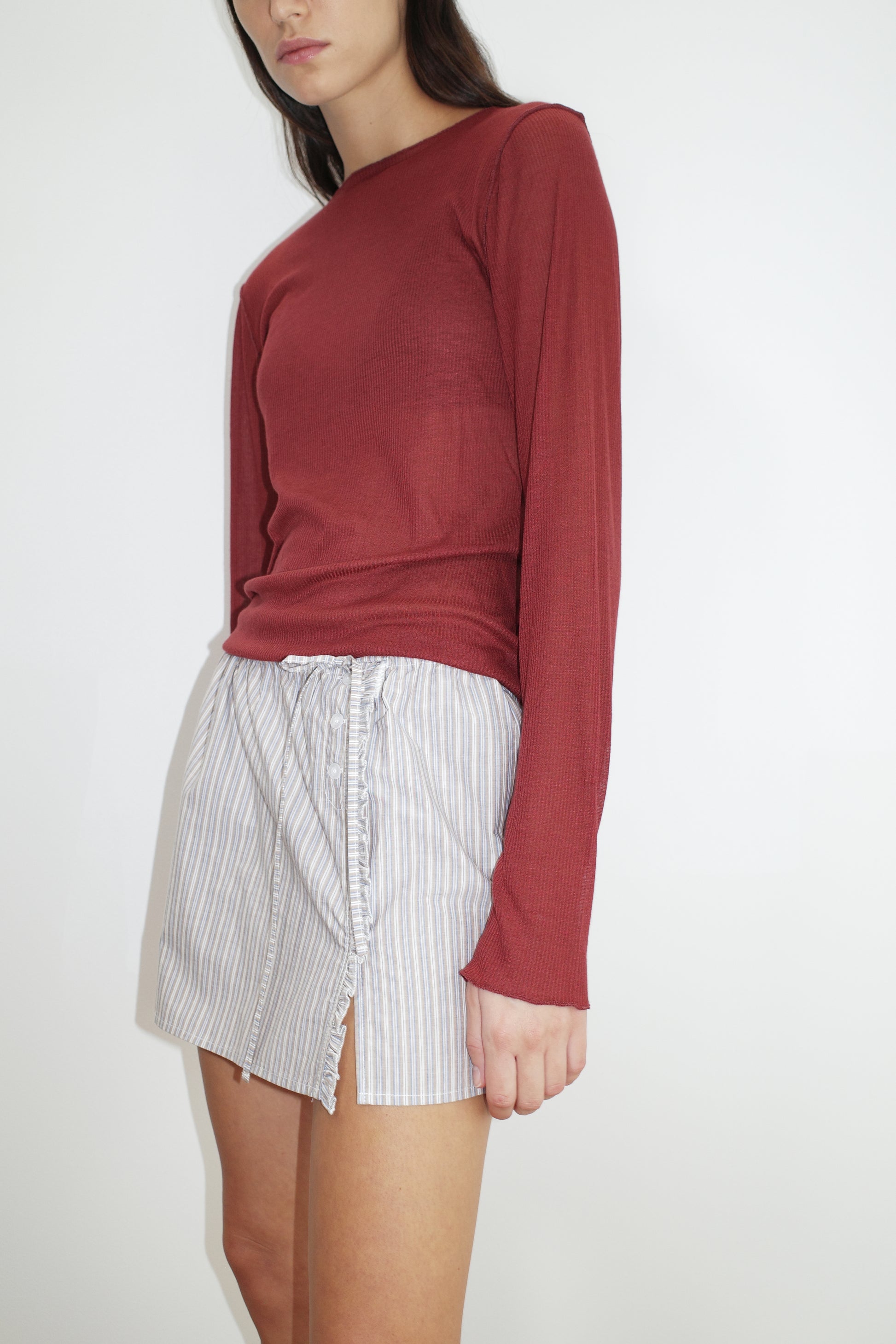 female model wears the ruffle mini skirt by Deiji Studios in seas stripe
simple mini skirt designed to sit at low waist features adjustable tie and ruffle edge on side with button detail
made from 100% GOTS certified organic cotton poplin
paired with a sheer knit long sleeve in crimson red