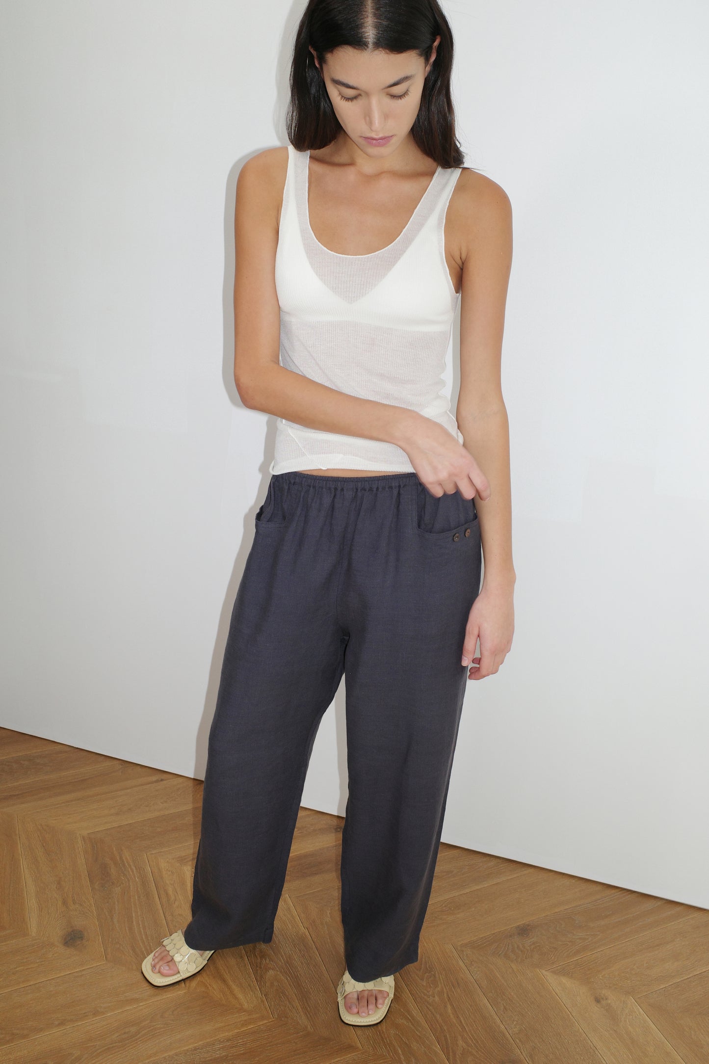 female model wears the linen square pocket pant by Deiji Studios in ink
an ankle length, straight leg pant features a soft minimal elastic waist with front seam pockets and button detail
made from 100% GOTS certified organic, OEKO-TEX 100 certified and EU certified stone washed french linen
paired with a white knit tank