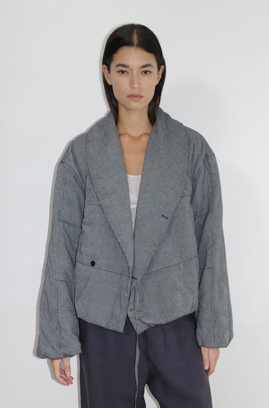 A woman with straight dark hair models the Exclusive Bubble Coat - Black White Stripe by 0, layering it over a light top and dark pants while standing against a plain white background.