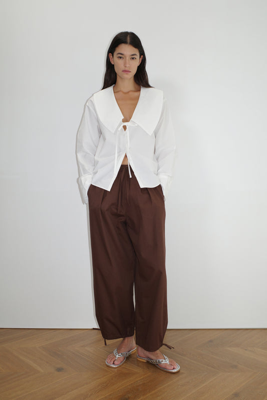 female model wears the collared tie shirt by Deiji Studios in white
a structured shirt features an oversized collar and cuff, tie at front collar opening, dropped shoulder and elongated sleeves in a boxy fit
made from 100% GOTS certified organic cotton poplin
paired with a brown cotton trouser