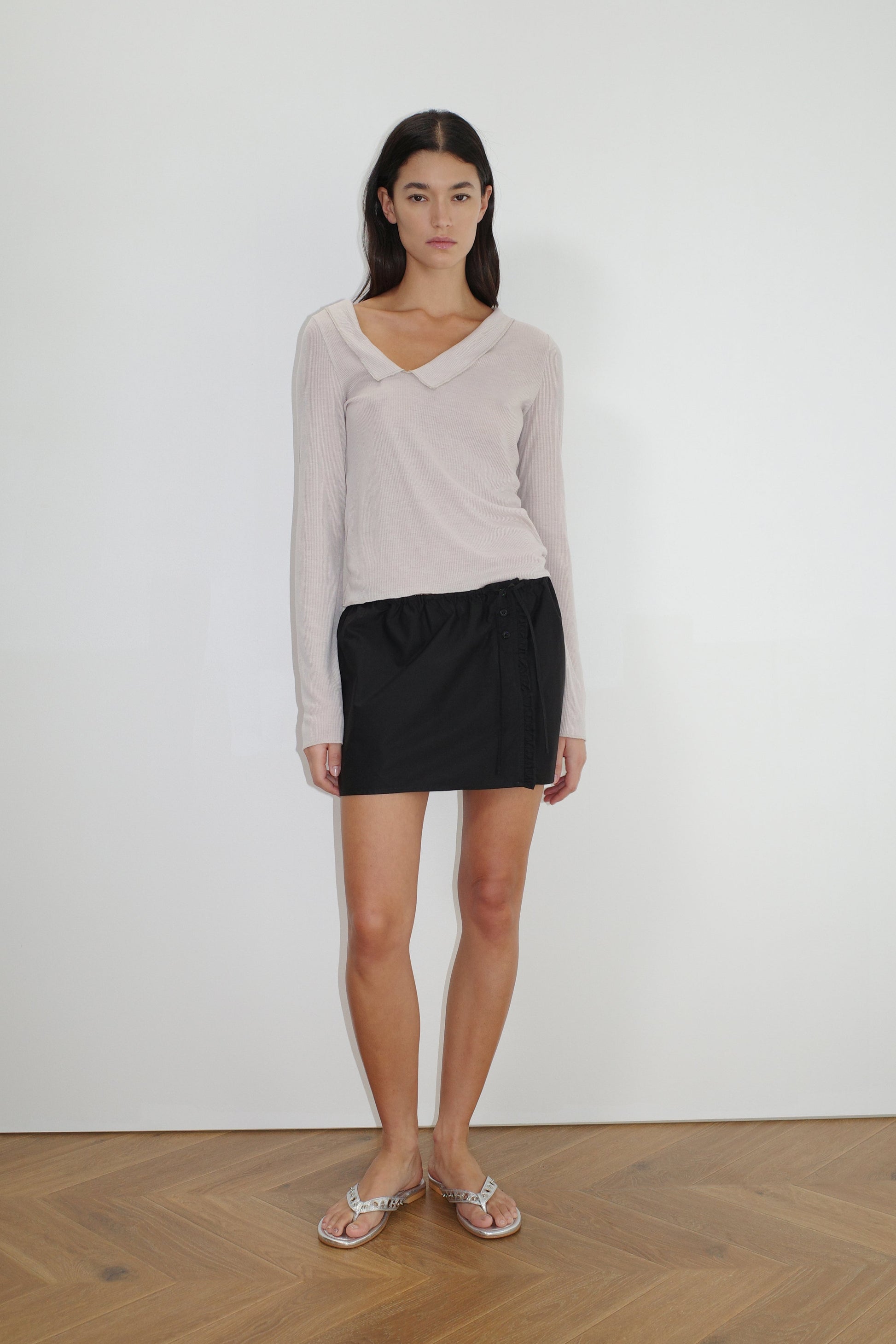 female model wears the ruffle mini skirt by Deiji Studios in black
simple mini skirt designed to sit at low waist features adjustable tie and ruffle edge on side with button detail
made from 100% GOTS certified organic cotton poplin
paired with a sheer knit long sleeve in beige