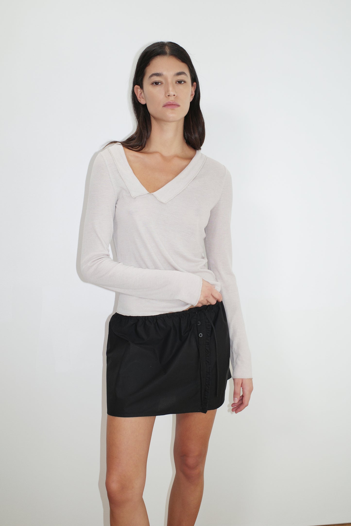 female model wears the ruffle mini skirt by Deiji Studios in black
simple mini skirt designed to sit at low waist features adjustable tie and ruffle edge on side with button detail
made from 100% GOTS certified organic cotton poplin
paired with a sheer knit long sleeve in beige