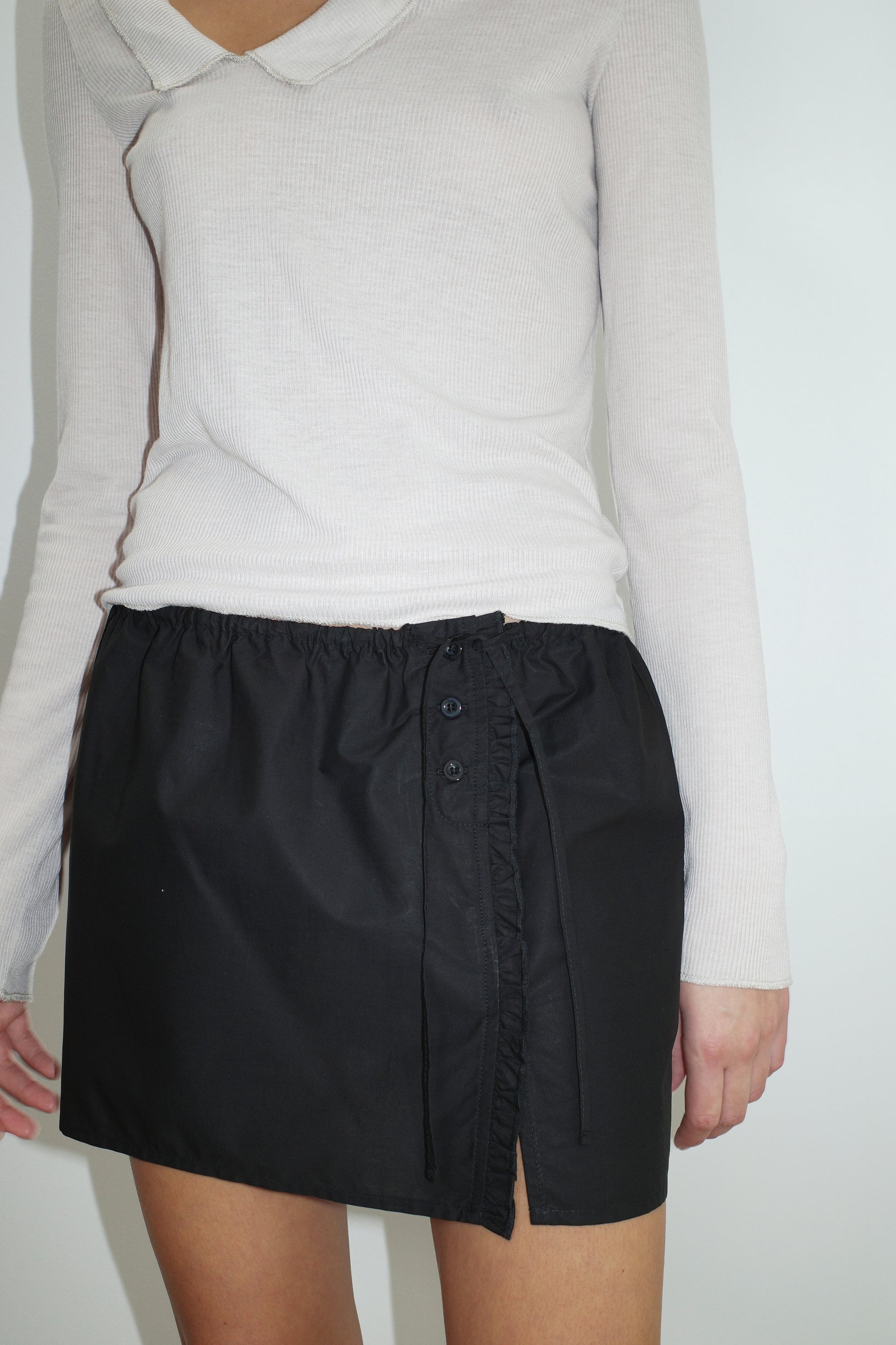 female model wears the ruffle mini skirt by Deiji Studios in black
simple mini skirt designed to sit at low waist features adjustable tie and ruffle edge on side with button detail
made from 100% GOTS certified organic cotton poplin
paired with a sheer knit long sleeve in beige