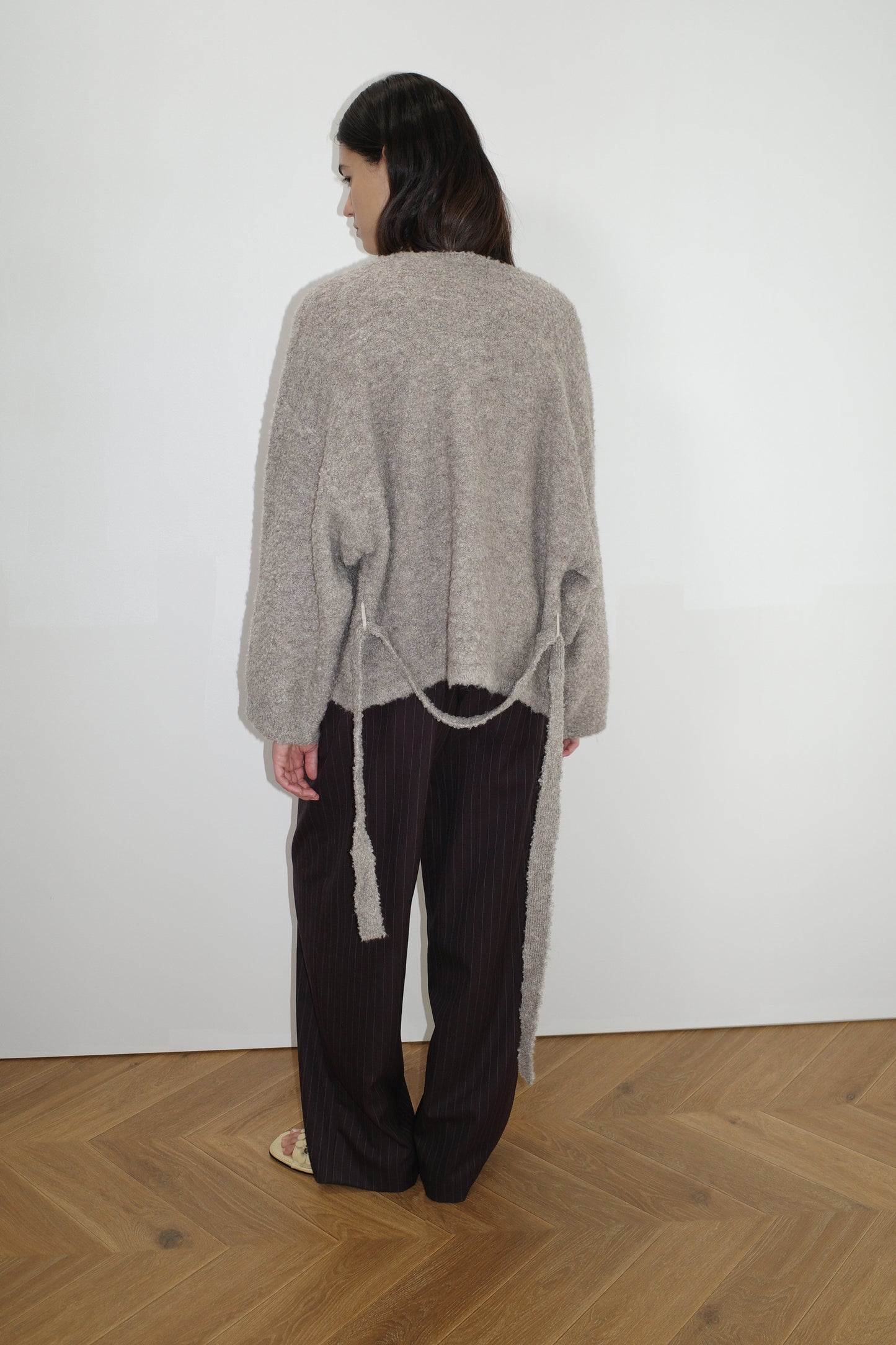 female model wears the pod knit by Deiji Studios in cloud grey
a relaxed and textured knit features a round shaped neckline with press stud front closure, removable self tie belt with long sleeves and high back neckline
made from a sustainable knit blend of 12% RWS certified wool, 30% recycled acrylic, 64% recycled polyester and 4% spandex
paired with a pinstripe wool pant