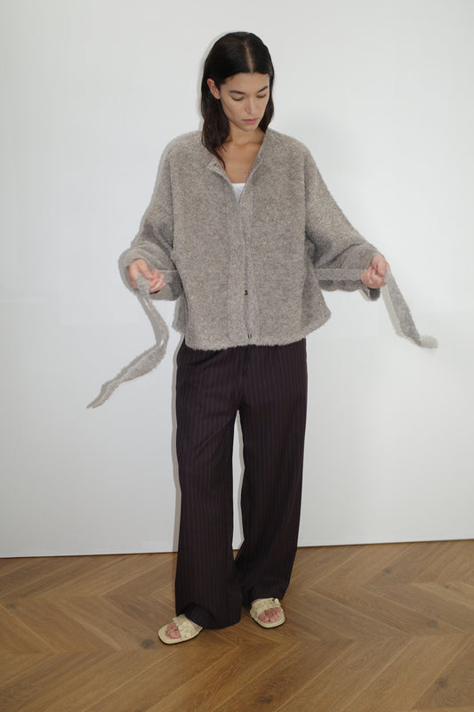 female model wears the pod knit by Deiji Studios in cloud grey
a relaxed and textured knit features a round shaped neckline with press stud front closure, removable self tie belt with long sleeves and high back neckline
made from a sustainable knit blend of 12% RWS certified wool, 30% recycled acrylic, 64% recycled polyester and 4% spandex
paired with a pinstripe wool pant