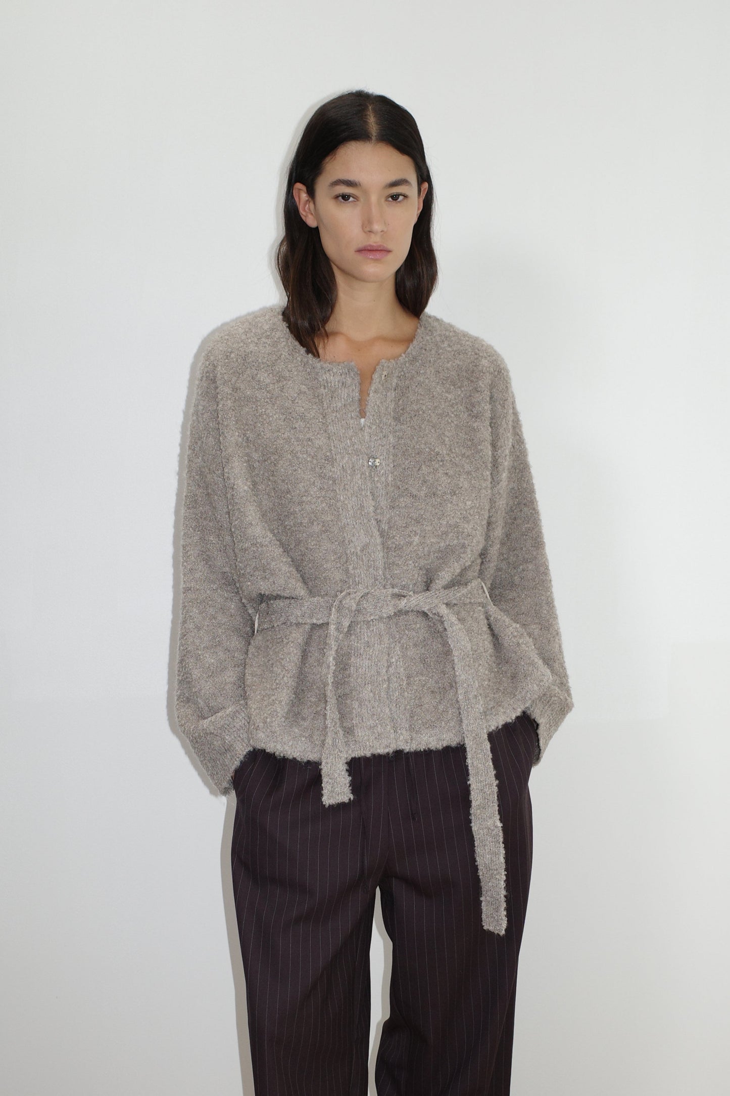 female model wears the pod knit by Deiji Studios in cloud grey
a relaxed and textured knit features a round shaped neckline with press stud front closure, removable self tie belt with long sleeves and high back neckline
made from a sustainable knit blend of 12% RWS certified wool, 30% recycled acrylic, 64% recycled polyester and 4% spandex
paired with a pinstripe wool pant