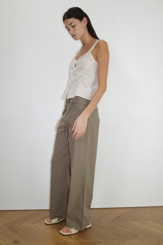 female model wears the ruffle button top by Deiji Studios in raquette stripe
a button up top featuring a butter base with mixed blue stripe, flattering v neckline, self-fabric ruffles along the straps and designed elasticated gatherings
made from 100% GOTS organic cotton
paired with a clay green pant