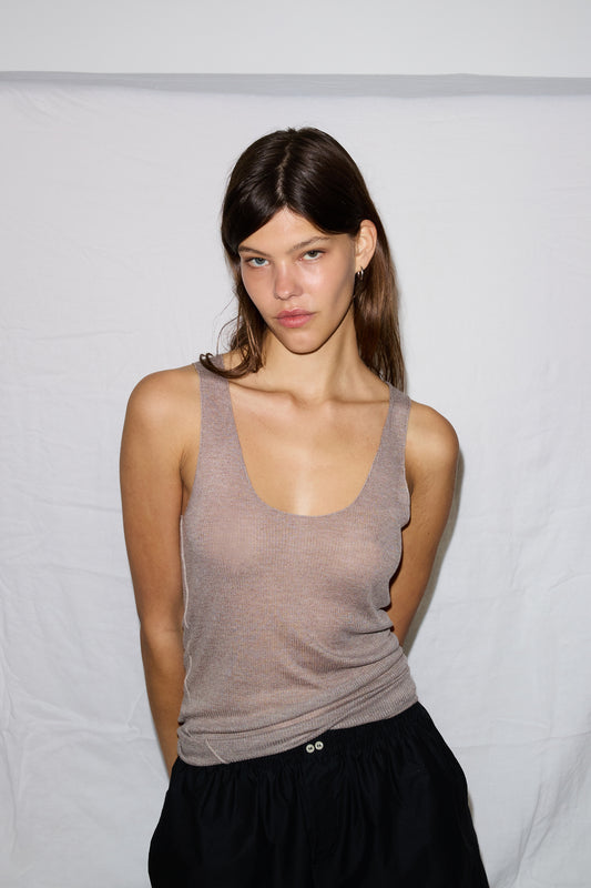 A young woman with straight brown hair stands before a white backdrop, wearing the Knit Tank in beige and black pants, facing the camera with a neutral expression.