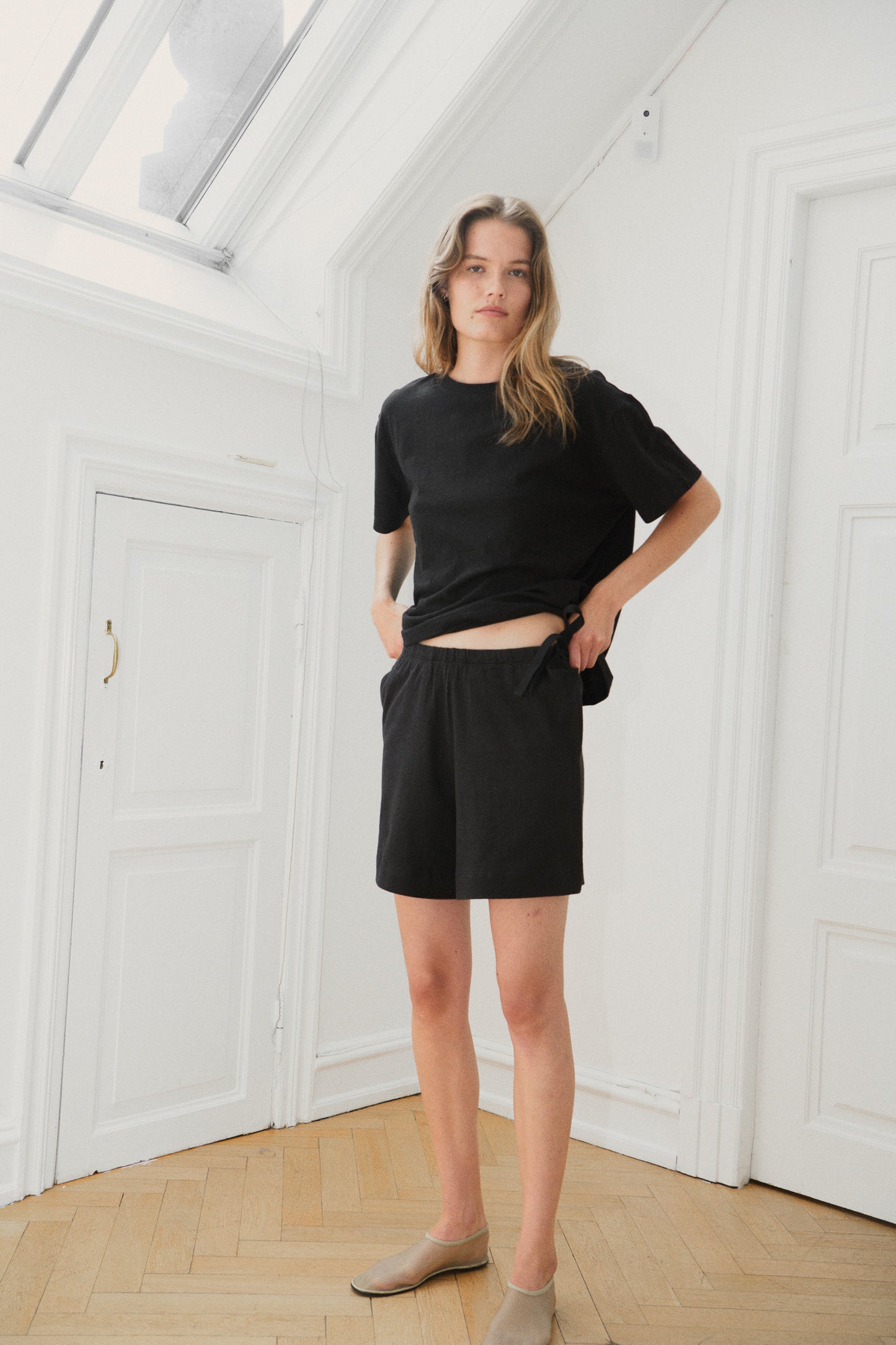 Female model wearing the leisure tee - black by Deiji Studios against plain background