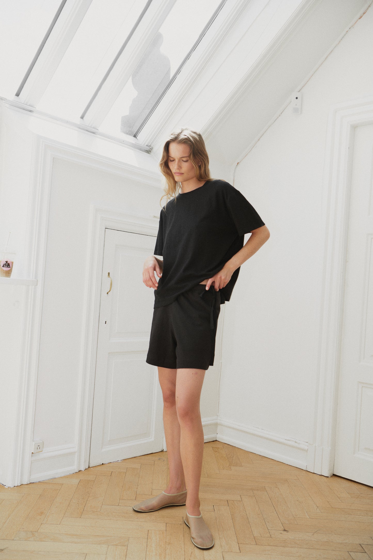 Female model wearing the leisure tee - black by Deiji Studios against plain background