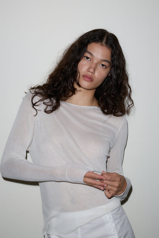 A young woman with long, wavy dark hair wears the Knit Long Sleeve in white and matching pants, standing against a plain white wall and looking at the camera with a neutral expression.