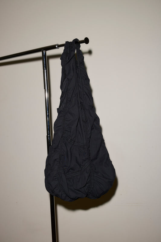 The Parachute Bag, featuring black ruched fabric, hangs from the end of a metal clothing rack against a plain off-white wall.