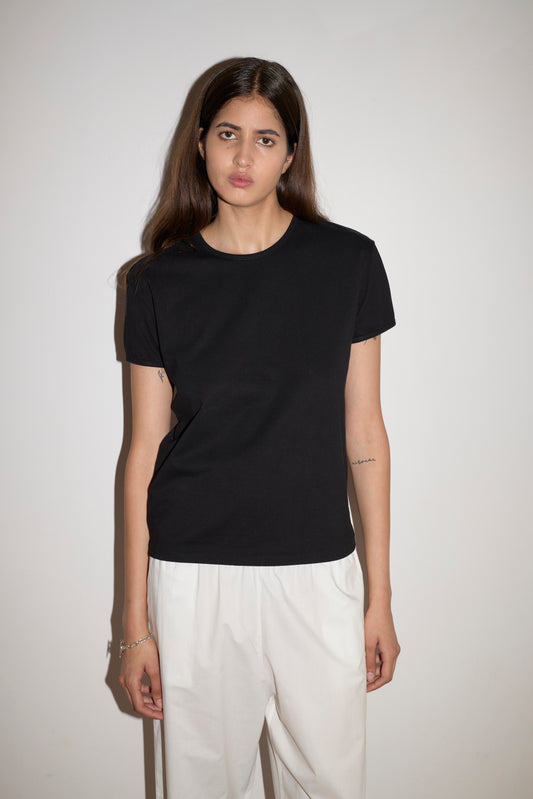 A woman with long brown hair stands against a white background, wearing the 0 Simple Tee - Black and white pants. She faces the camera with a neutral expression.