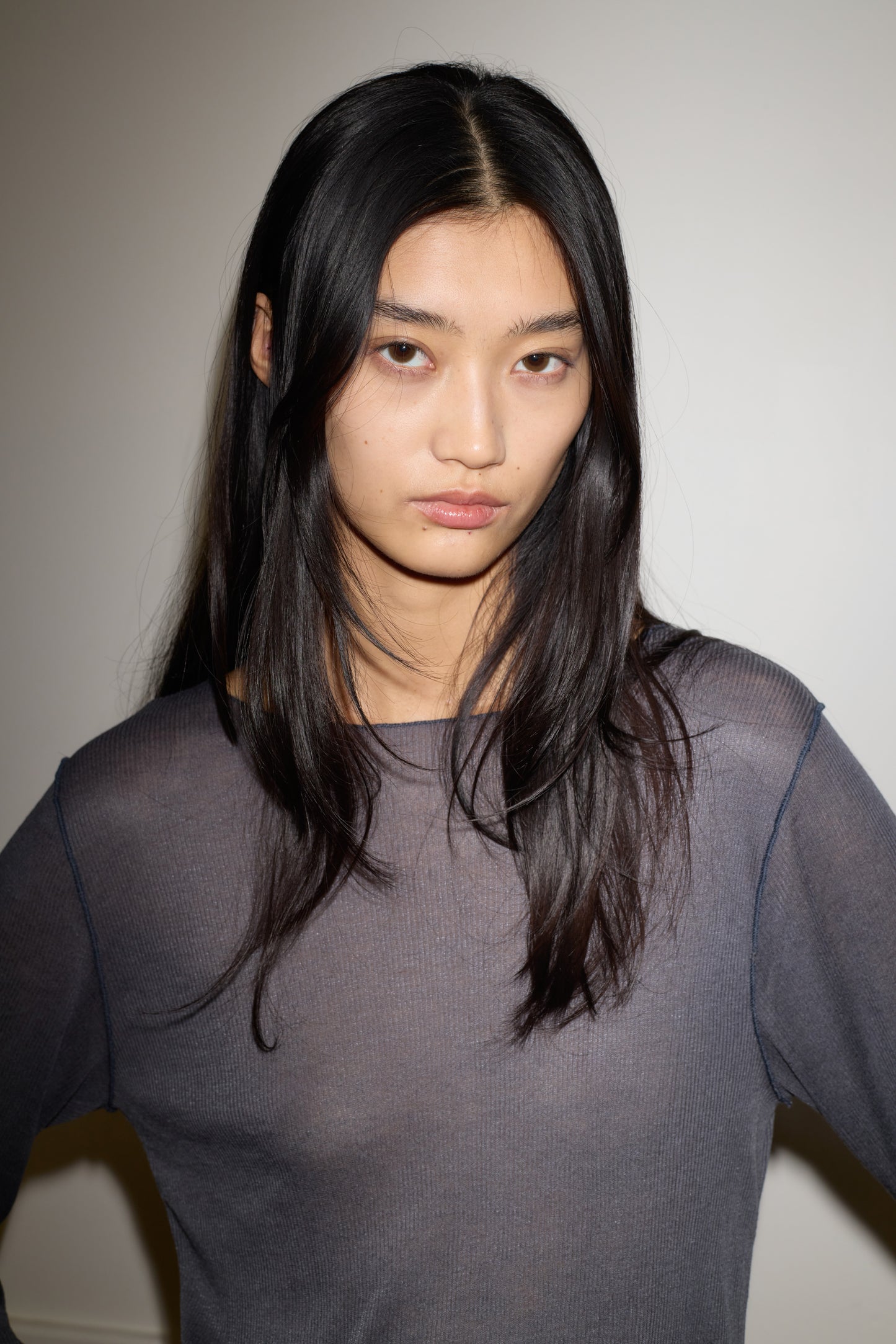 A young woman with long, straight black hair and a neutral expression stands against a plain white background, wearing the Knit Long Sleeve - Steel by 0.