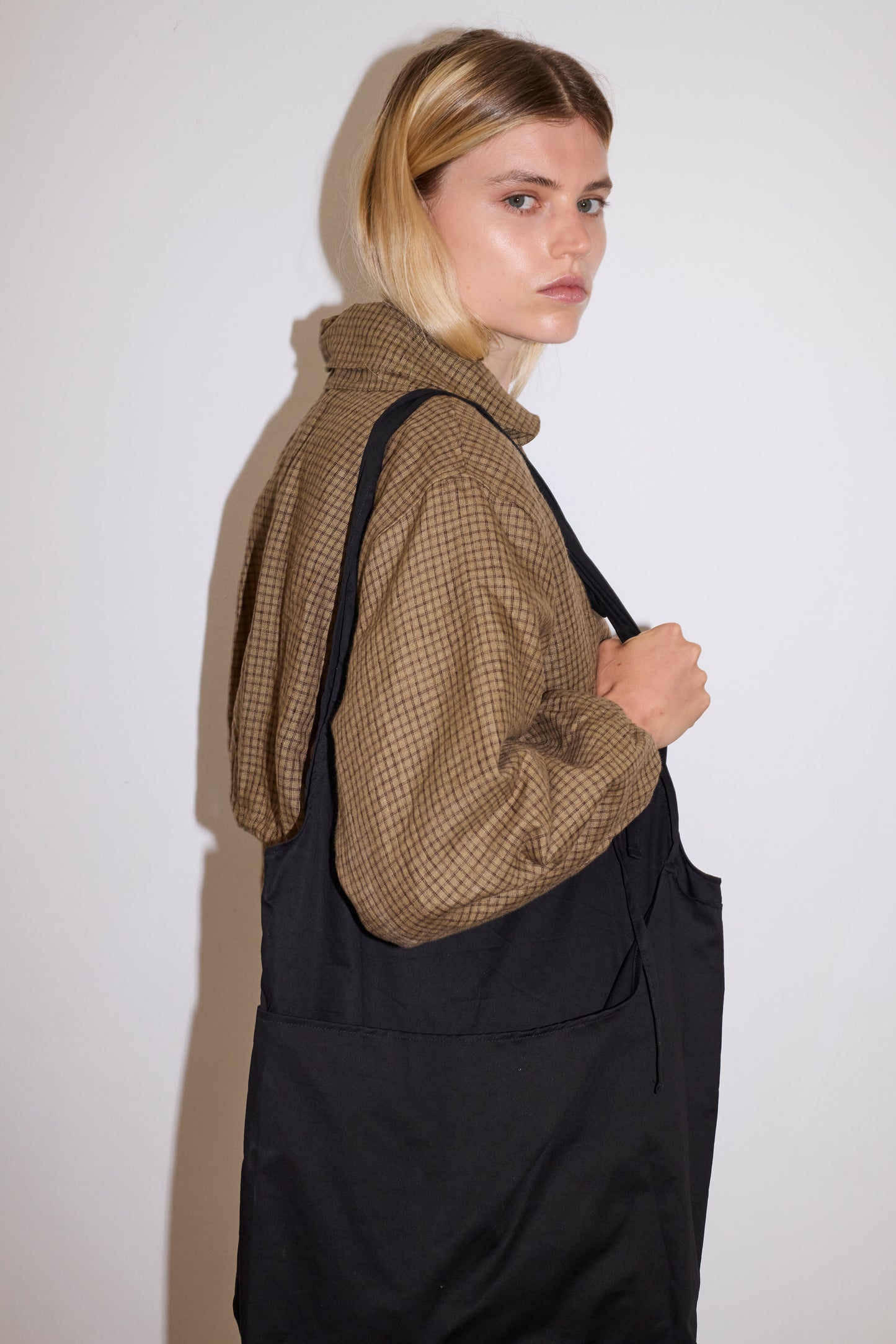 blonde female model wears a black elevated, medium weight double layered tote featuring fixed shoulder straps with a tie detail and flat base paired with a black and brown gingham print zip up cotton jacket