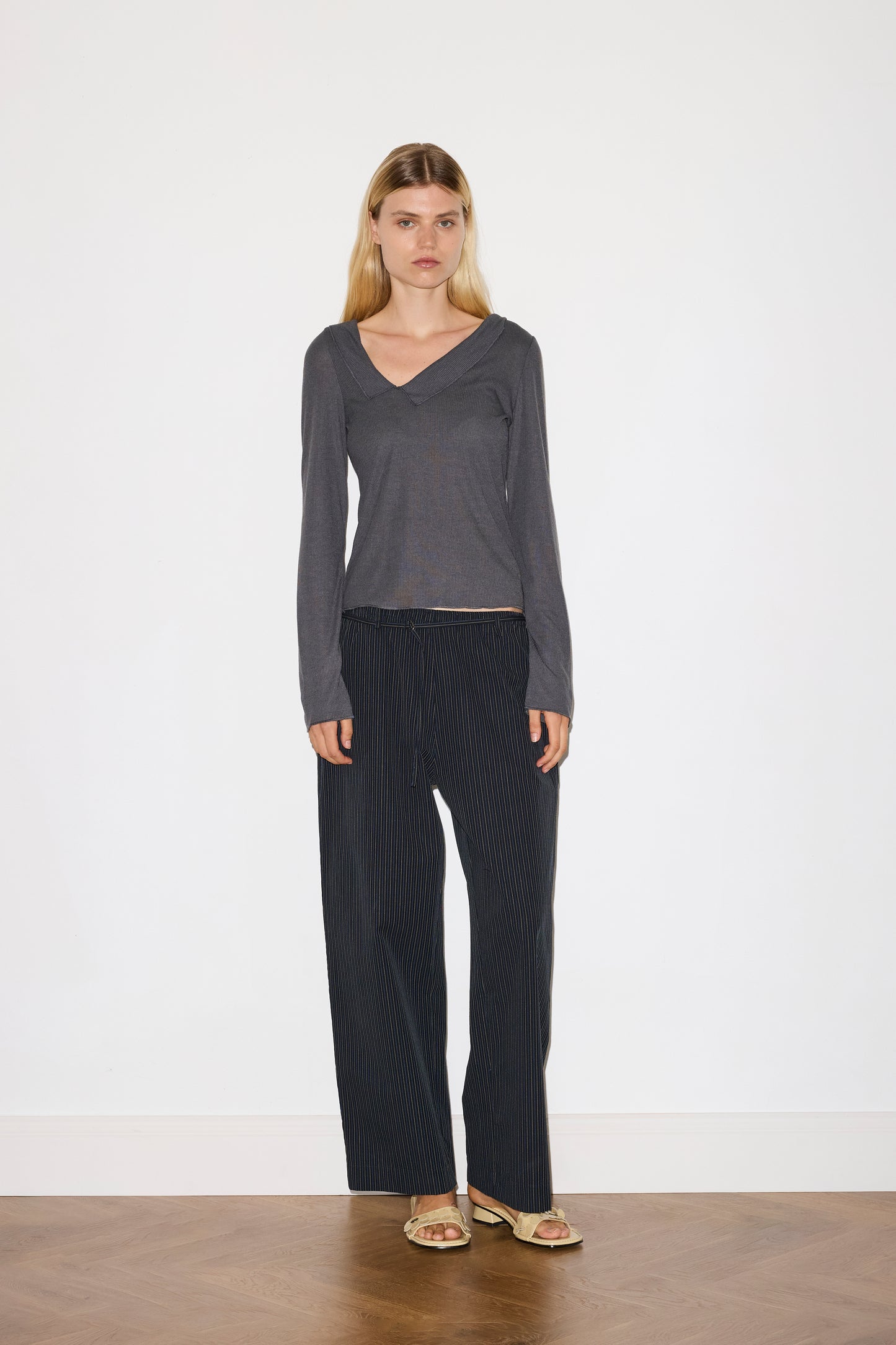 blonde female model wears grey long sleeve top, worn with a navy and yellow striped trouser