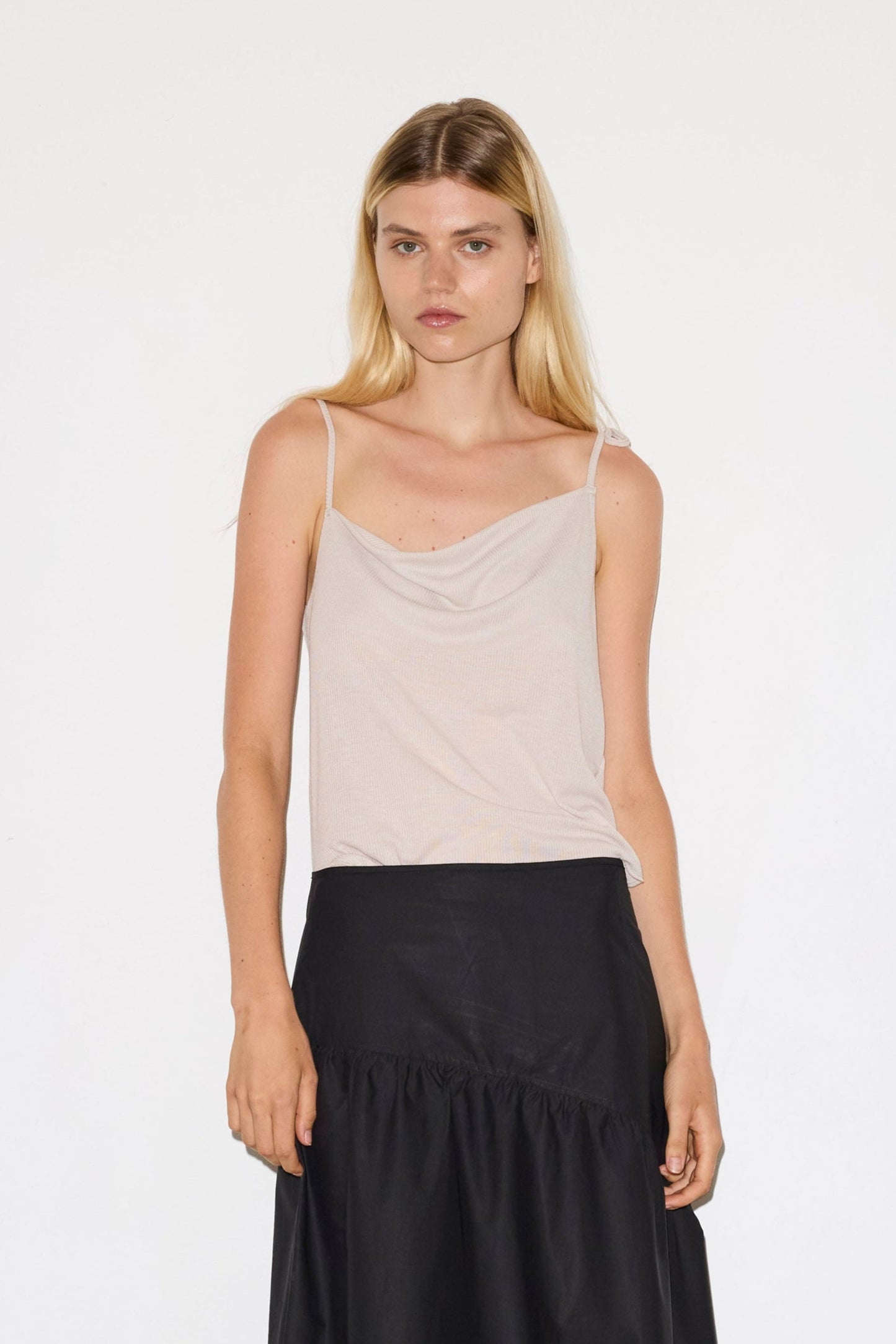 female model wears the split top by Deiji Studios in shell
a sheer fine knit relaxed tank with a fold over cowl neckline and low draping back, features self fabric rouleau straps, baby lock hem finishes and a asymmetric bottom detail
made from a responsible blend of 85% Recycled Polyester and 15% Viscose
paired with a black cotton skirt