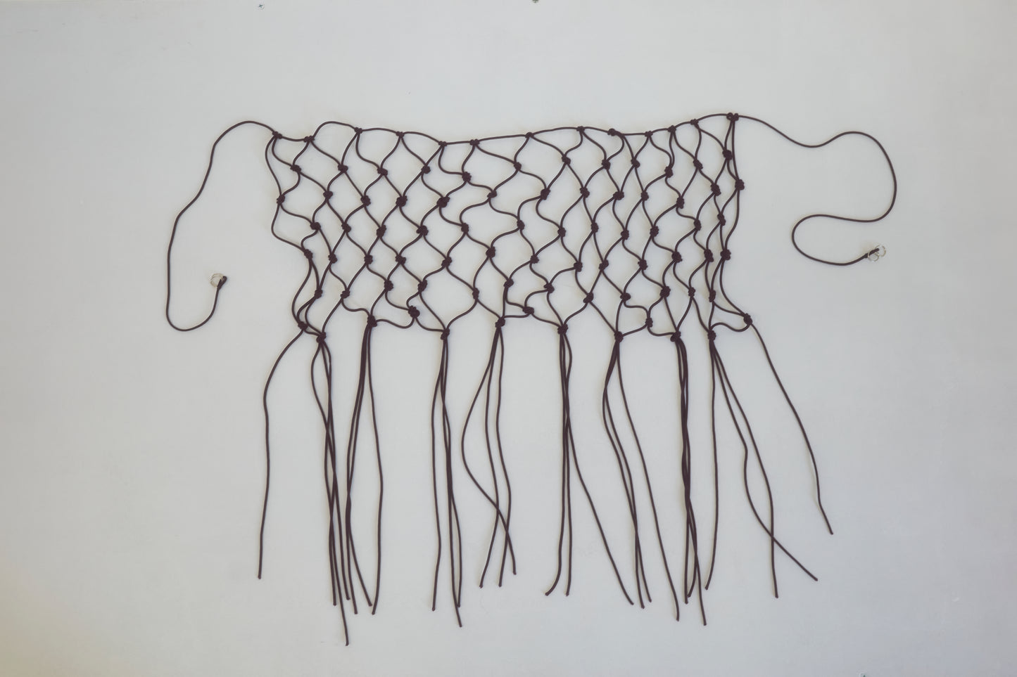 A handwoven black macramé belt made from recycled polyester, featuring loose ends and fringes, displayed flat on a white background.