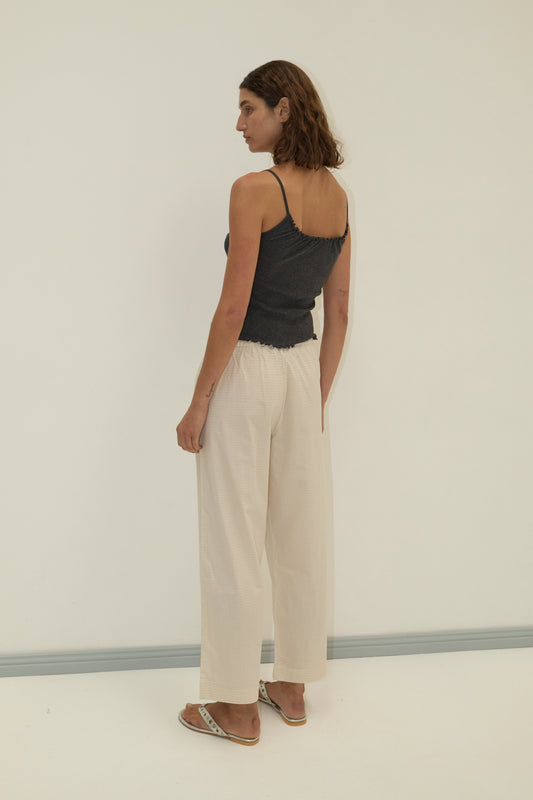 A person with short brown hair, wearing the Wool Blend Flounce Tank - Grey from Deiji Studios, loose light-colored pants, and sandals stands slightly turned away from the camera against a plain light background.