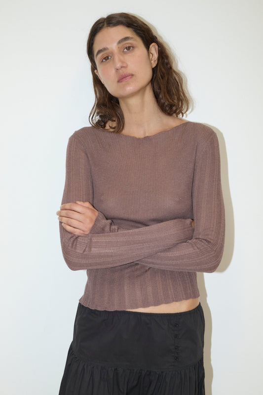 A woman with wavy brown hair stands against a white background, wearing the Open Work Longsleeve - Hazel and a black skirt. She crosses her arms and has a neutral expression.