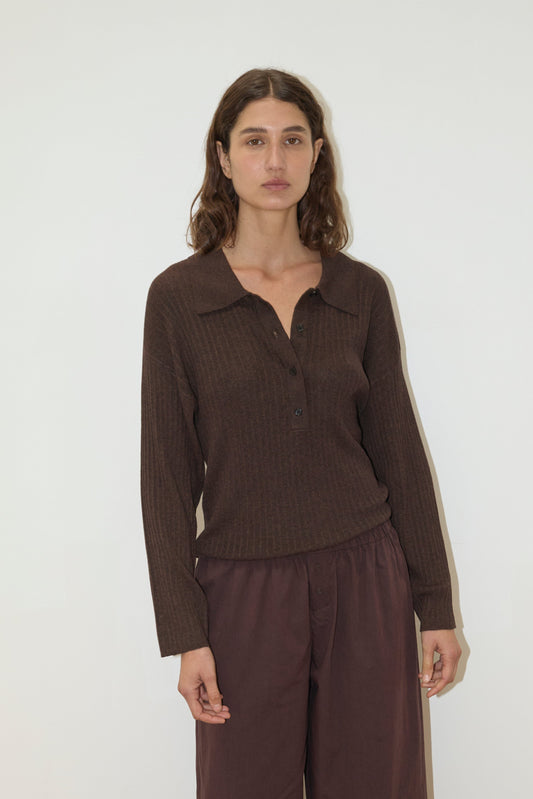 A model wears the Polo Knit - Dark Almond by Deiji Studios with dark burgundy wide-leg trousers, set against a white background.