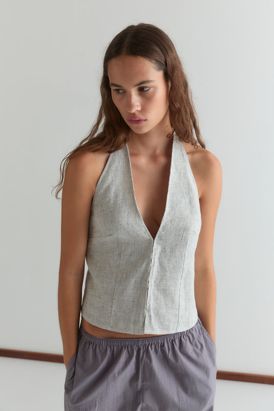 A woman with long brown hair wears Deiji Studios' Close Halter Top - Fine Stripe and loose striped gray pants, standing against a plain white background with her hands in her pockets.