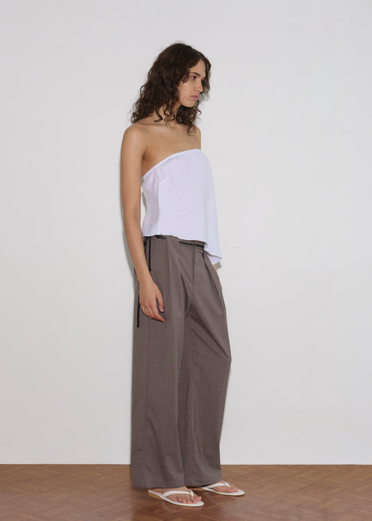 A woman poses sideways against a light grey wall wearing a white strapless tube top, Belt Loop Pant - Grey Pink Stripe, a thin black belt, and white flip-flops.