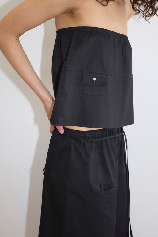 A person models the Pocket Skirt - Black, a strapless, loose-fitting skirt with a front pocket, against a white background. Only the upper body and part of the lower body are visible.