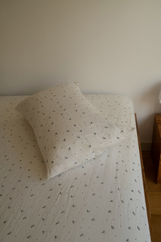 A neatly made bed with vintage floral Sheets in a simple, softly lit room featuring a white pillowcase and a wooden nightstand.