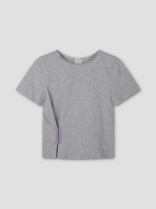 The Pinch Tee - Grey is a relaxed, light gray short sleeve crop top with a round neckline and a small purple tag at the bottom left hem, shown against a matching light gray background.