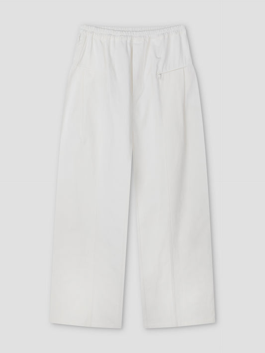 The Pleat Pant - White features a relaxed straight-leg fit with an elasticated waistband, side pockets, a small zip pocket, and subtle front seam details, shown flat on a light grey background.