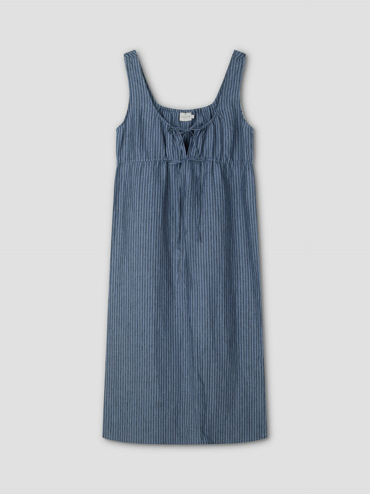 The Sleeveless Cord Dress - Azure Stripe by Deiji Studios features thin vertical white stripes, a scoop neckline, front tie detail, and a relaxed midi silhouette. Displayed on a plain light gray background.