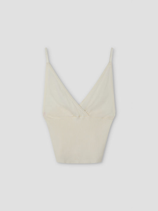 The Cross Panel Knit Top - Off White features a cream hue, thin spaghetti straps, and a deep V neckline in a cross-panel knit style inspired by Deiji Studios, shown against a plain light gray background.