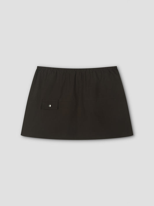 The Pocket Skirt is a plain black mini skirt with an elastic waistband and a small flap pocket with a button on the left side, shown on a light gray background.