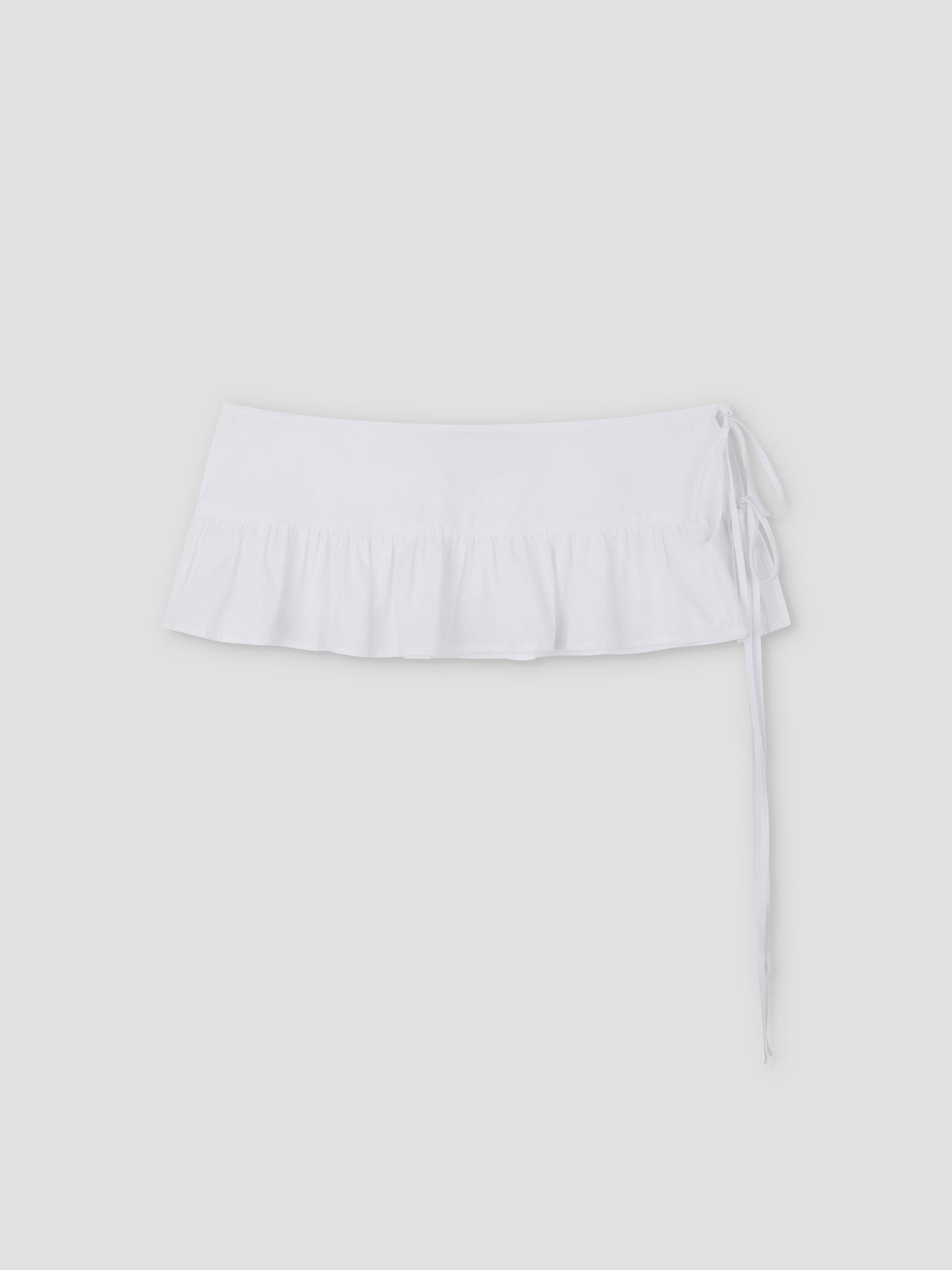 The Flounce Belt is a white mini skirt featuring a ruffled hem and side tie, shown against a plain light gray background.