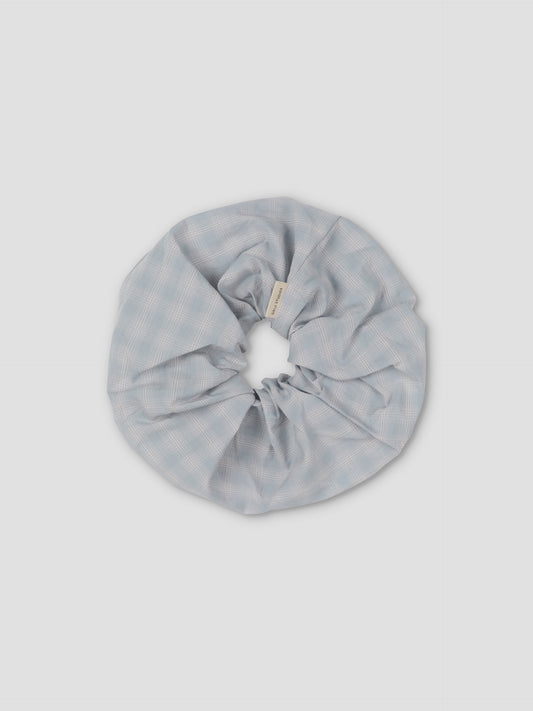 The Scrunchie is a large, light blue hair accessory with a subtle checkered pattern, shown on a plain light gray background.