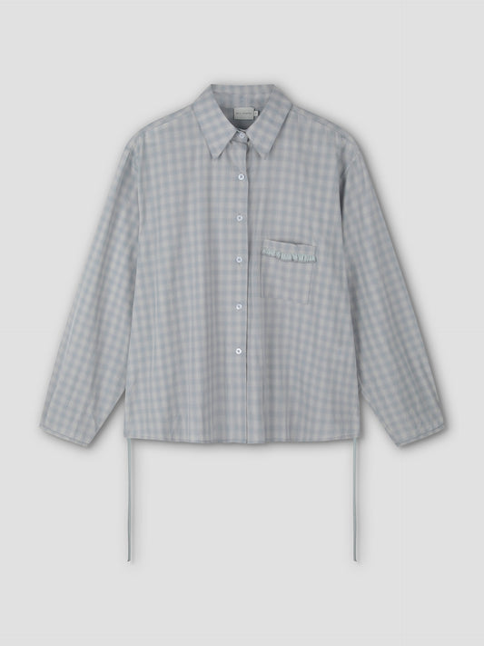 The Day Shirt - Blue Check features a light blue and white gingham pattern, boxy fit, collar, long sleeves, chest pocket with ruffle detail, and two thin side ties near the bottom hem.