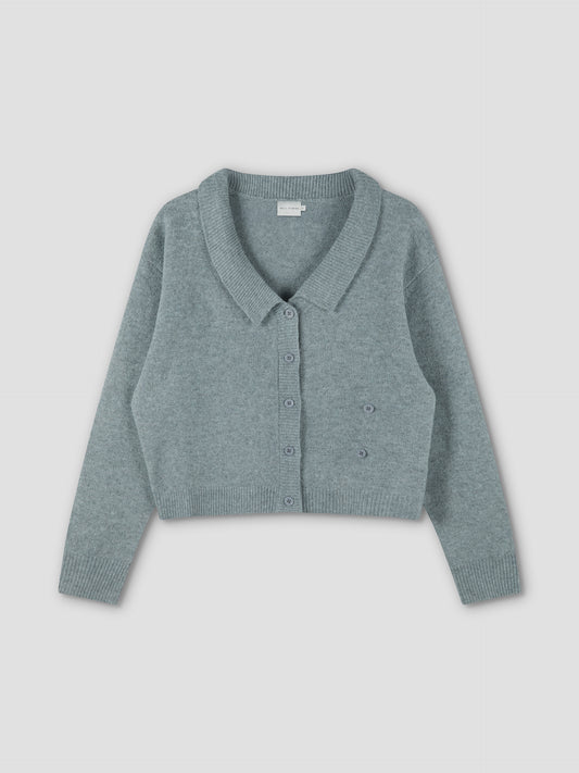 The Cross Button Cardigan - Ice Blue from Deiji Studios is a soft knit, light blue-green cropped cardigan with long sleeves, ribbed hem and cuffs, wide collar, and front cross button closure. Shown laid flat on a white background.