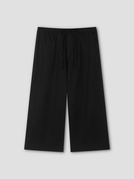 The Mid Pocket Short - Black by Deiji Studios features a relaxed, wide-leg fit with an elastic waistband, drawstring, and a visible right-side pocket. Displayed flat on a light gray background, these shorts evoke a comfortable 3/4 length style.
