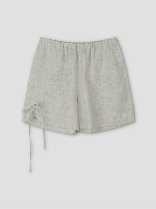 The Eyelet Short - Fine Stripe features a light gray linen, elastic waistband, and a decorative left tie, shown on a plain light background. Inspired by Deiji Studios' signature relaxed style.