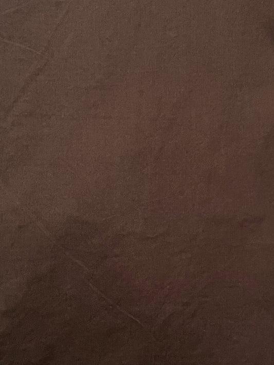 A close-up of chocolate brown fabric, revealing subtle creases and textured detail—evoking the relaxed feel of the Ease Trouser - Chocolate by Deiji Studios.