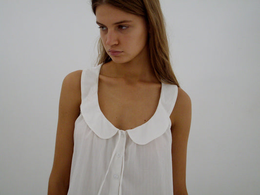A young woman with long brown hair wears the Round Collar Top - White Texture by Deiji Studios, looking slightly down and to the side against a plain white background.