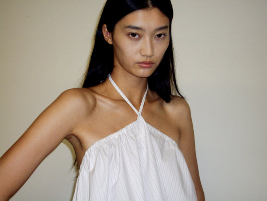A person with long dark hair and a neutral expression wears the Napkin Top - Pacific Stripe by Deiji Studios, standing against a plain light-colored wall.
