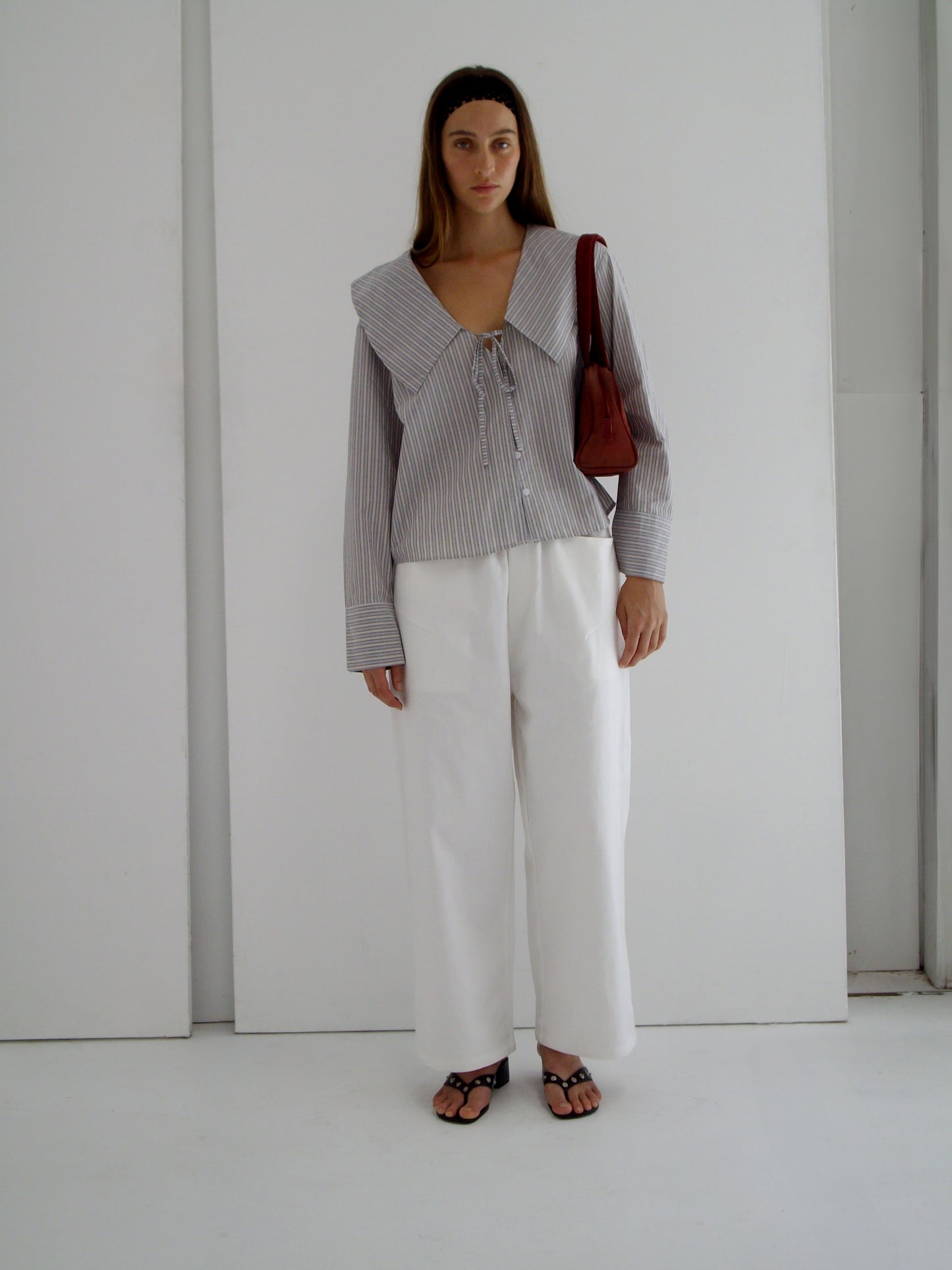 female model wears the collared tie shirt by Deiji Studios in seas stripe
a structured shirt features an oversized collar and cuff, tie at front collar opening, dropped shoulder and elongated sleeves in a boxy fit
made from 100% GOTS certified organic cotton poplin
paired with a white cotton trouser