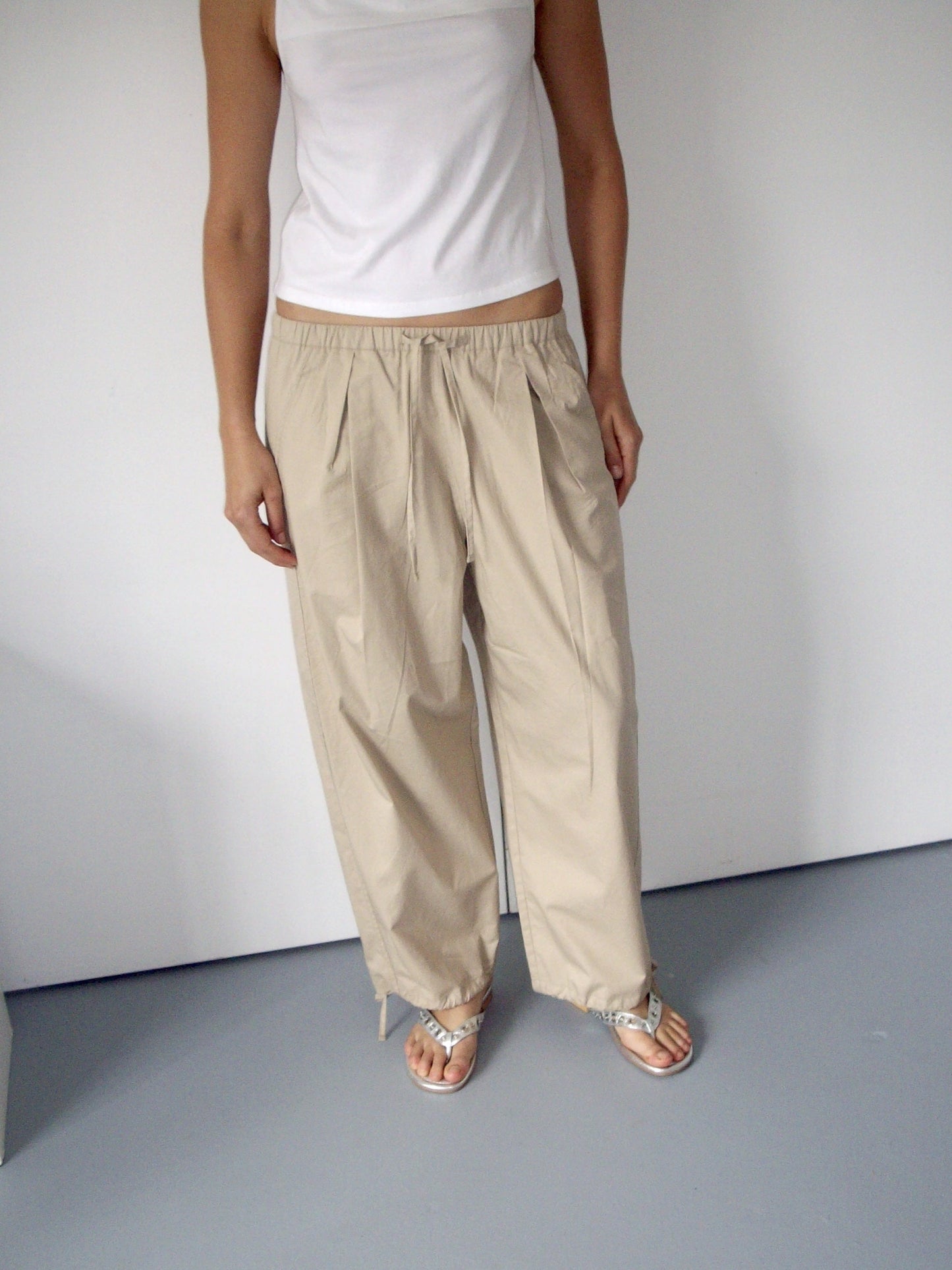 female model wears beige soft cotton trouser featuring a drawcord hem and waist with deep side pockets designed to sit mid-low waist for a relaxed look and made from 100% GOTS certified organic cotton.