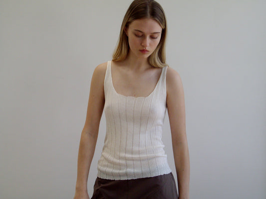 A young woman with long, straight hair wears the Open Work Tank and dark pants, standing against a plain light background while looking down.