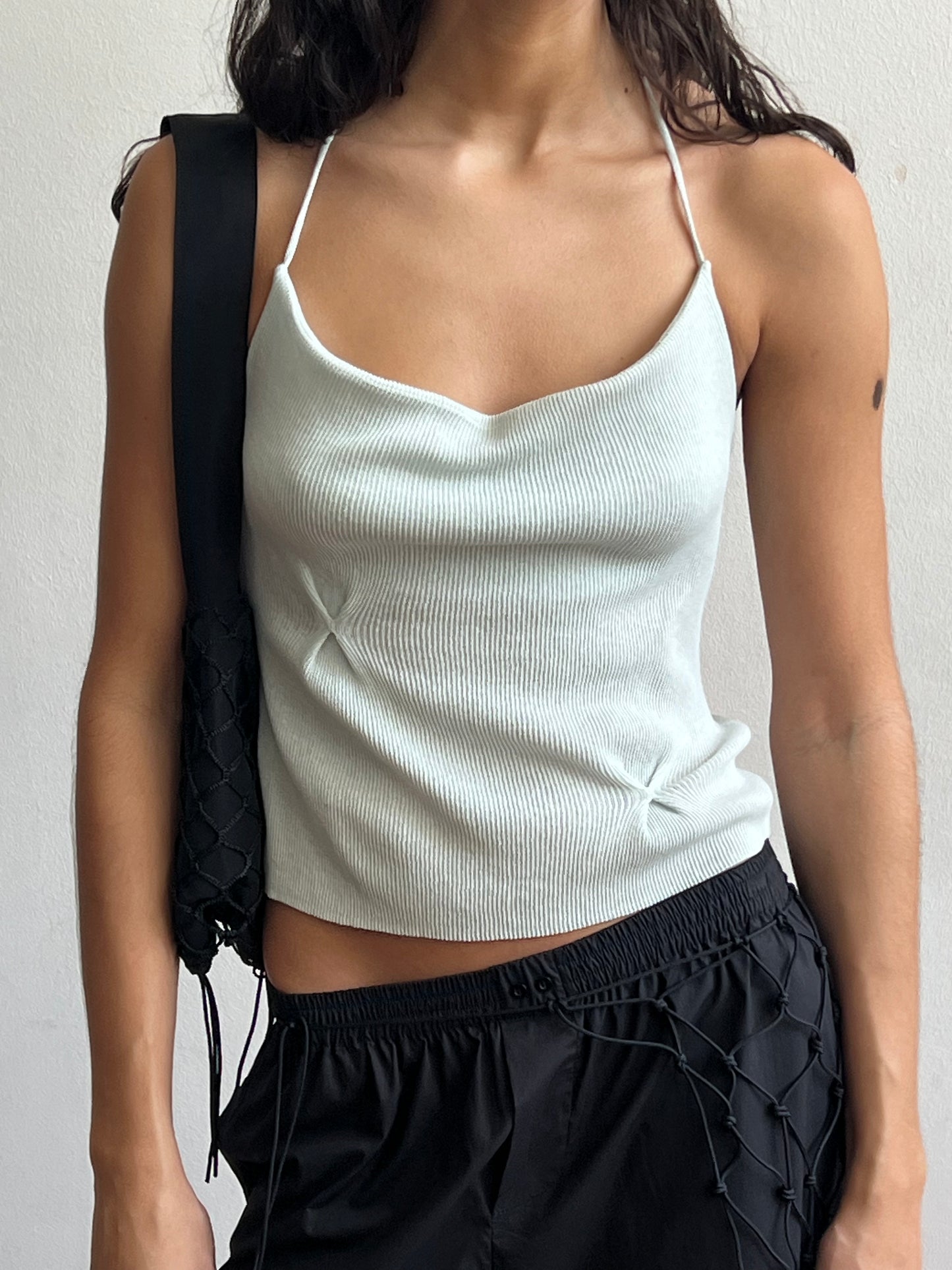 A woman wears the Fine Knot Tank in Ice Blue with thin straps and a tailored fit, styled with black wide-leg pants featuring mesh net details and a black woven shoulder bag.